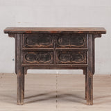 Vintage wooden side table with four drawers against a light gray wall.