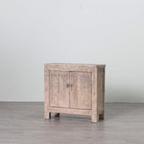 A small rustic wooden cabinet with two doors and round metal knobs, shown on a gray floor against a white wall.