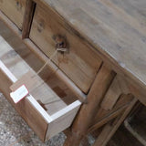 A rustic wooden sideboard or console table with two drawers, one of which is open, set on a speckled concrete floor.