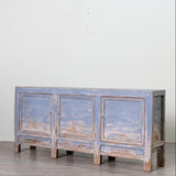 A rustic three-door sideboard cabinet with a distressed blue-gray finish, standing on a light gray wood floor against a plain off-white wall.