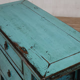 Vintage turquoise wooden chest with peeling paint on a wooden surface.