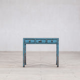 Blue distressed console table on a light wooden floor with a white wall background
