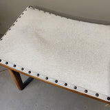 White upholstered bench with wooden legs and nailhead trim on a gray floor.