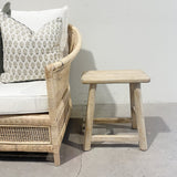 Wicker chair with a cushion and wooden stool against a plain wall.