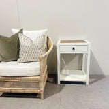 Wicker chair with cushions next to a white nightstand against a plain wall.