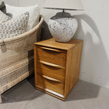 Wooden nightstand with a textured lamp next to a wicker chair with cushions.