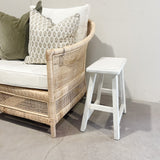 Wicker chair with cushions and a white stool against a plain wall.