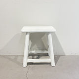 White wooden stool against a plain white wall.