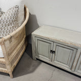 Wicker chair with patterned cushion next to a wooden cabinet against a white wall.