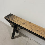 Wooden bench with blackened edges against a white wall