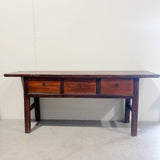 Wooden table with three drawers against a white wall