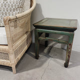 Wicker chair and vintage green wooden table against a white wall.