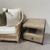 Wicker chair with cushions and a wooden side table against a plain wall.