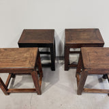 Four wooden stools of varying sizes on a plain floor.