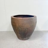 Large brown ceramic pot on a white floor with a white wall background