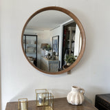 Round wooden-framed mirror on a white wall above a wooden dresser with decorative items.