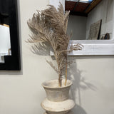 Decorative plant in a stone vase on a wooden surface with a neutral background
