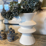 Decorative items including a white urn, blue and gold jar, and greenery on a textured surface.