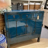 Blue wooden cabinet with three drawers and two doors in a room setting.
