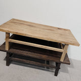 A rustic two-tier wooden coffee table with a light natural wood top and a dark brown lower shelf, photographed against a plain white wall and concrete floor.