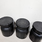 Three rustic black-painted log stumps with visible wood grain and tree-ring patterns, arranged against a plain white wall.