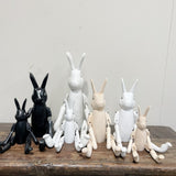 A collection of wooden rabbit figurines in various sizes displayed on a wooden surface, with colors including black, white, and natural wood tones.