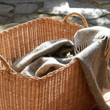 Wicker basket with a blanket inside, placed outdoors on stone pavement.