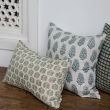 Three patterned pillows on a wooden surface with a white wall and decorative element in the background.