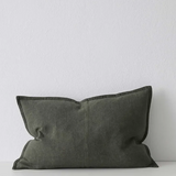 An olive green rectangular lumbar pillow with a textured fabric cover and dark piping, resting on a white surface against a white wall.