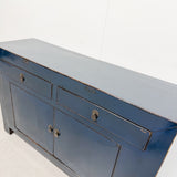 A blue painted wooden sideboard or credenza with distressed edges, featuring two small top drawers and two larger lower cabinet doors with round metal knobs, photographed against a plain white wall.