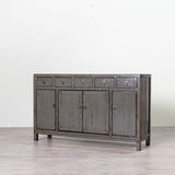 A rustic, weathered gray wooden sideboard cabinet with five drawers on top and four doors below, set against a plain white wall and light gray floor.