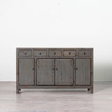 A distressed gray wooden sideboard cabinet with five drawers on top and three doors below, set against a plain white wall and light gray floor.