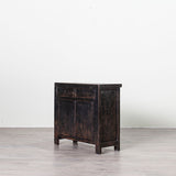 A dark, distressed wooden cabinet with two small top drawers and two larger lower doors, standing on a light gray floor against a white wall.
