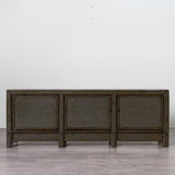 A dark gray wooden sideboard with three cabinet doors, shown against a plain white wall and light gray floor.