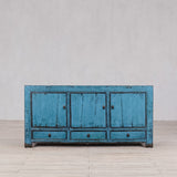 Blue distressed wooden cabinet on a light wooden floor with a gray wall background