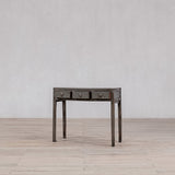 Wooden desk with three drawers on a wooden floor against a plain wall
