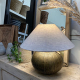 Decorative lamp with a textured shade on a wooden surface, surrounded by wicker baskets and a mirror.