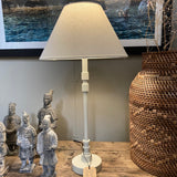 Table lamp with beige shade on a wooden surface next to decorative figures and a woven basket.