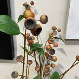 Decorative branch with acorn-like fruits and green leaves on a white surface.