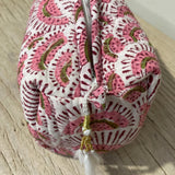 Pink and white patterned fabric bag with a tassel on a wooden surface