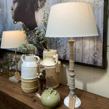 Decorative lamp with a white shade on a wooden surface with a patterned wall in the background.