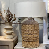Decorative lamp with wicker base and white shade on a wooden surface.