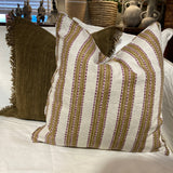 A decorative throw pillow with horizontal stripes in brown, beige, and white, styled on a bed alongside a textured olive green blanket.