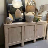 Light wooden sideboard with decorative items including a lamp, piggy bank, and plants.