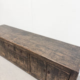 A rustic dark brown wooden sideboard or credenza with distressed weathered finishes, shown from an elevated angle against a plain white wall.