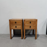 Two matching wooden two-drawer nightstands with dark metal ring pulls, shown side by side against a plain white wall and concrete floor.