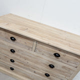 A light natural wood dresser with multiple drawers and black oval knobs, photographed against a plain white wall.