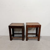 A pair of dark brown wooden side tables with woven cane tops, set against a plain white wall and concrete floor.