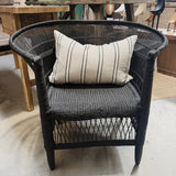 A dark woven wicker accent chair with a cream throw pillow featuring black stripes, set in a rustic furniture store.