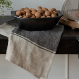 Black bowl filled with walnuts on a textured surface with a towel.